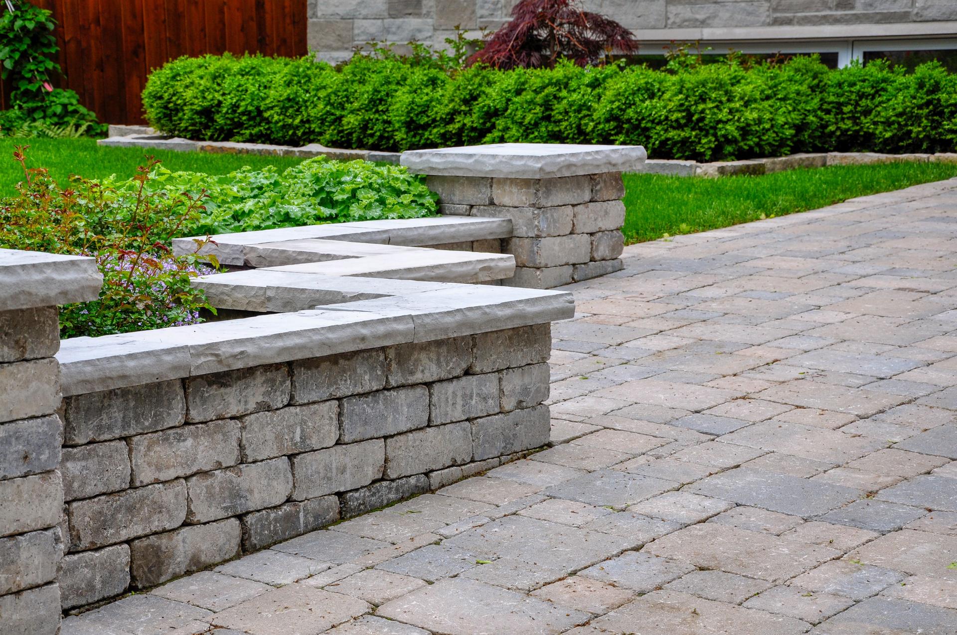 A tumbled paver retaining wall with natural stone coping defines a driveway.